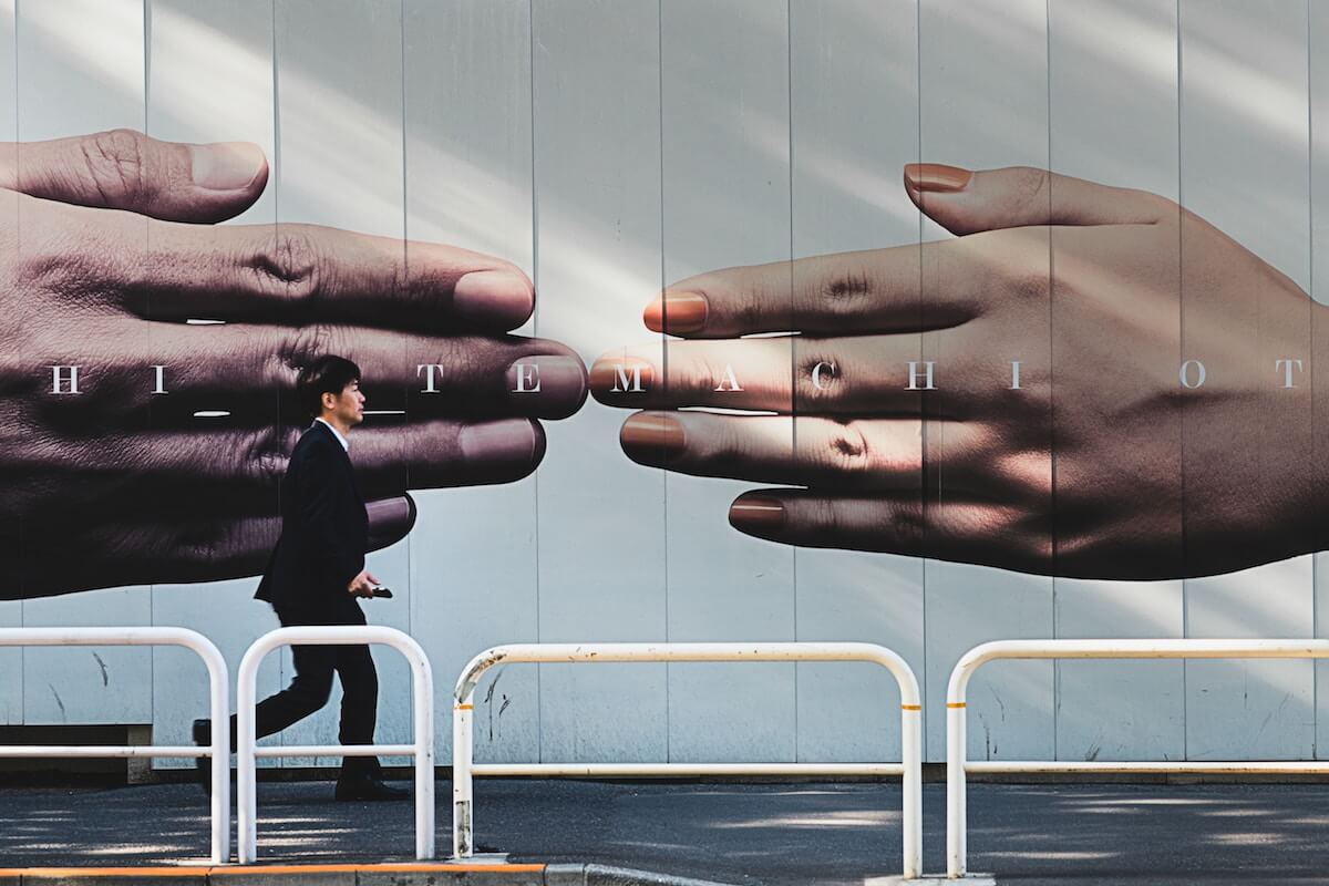 Asian man walking by a billboard of two hands